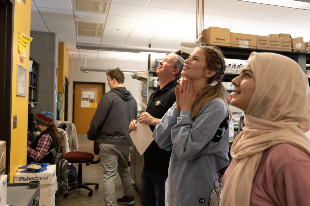 Dr. Michael Guy and lab students look towards commemorative "obituaries" of former lab students.